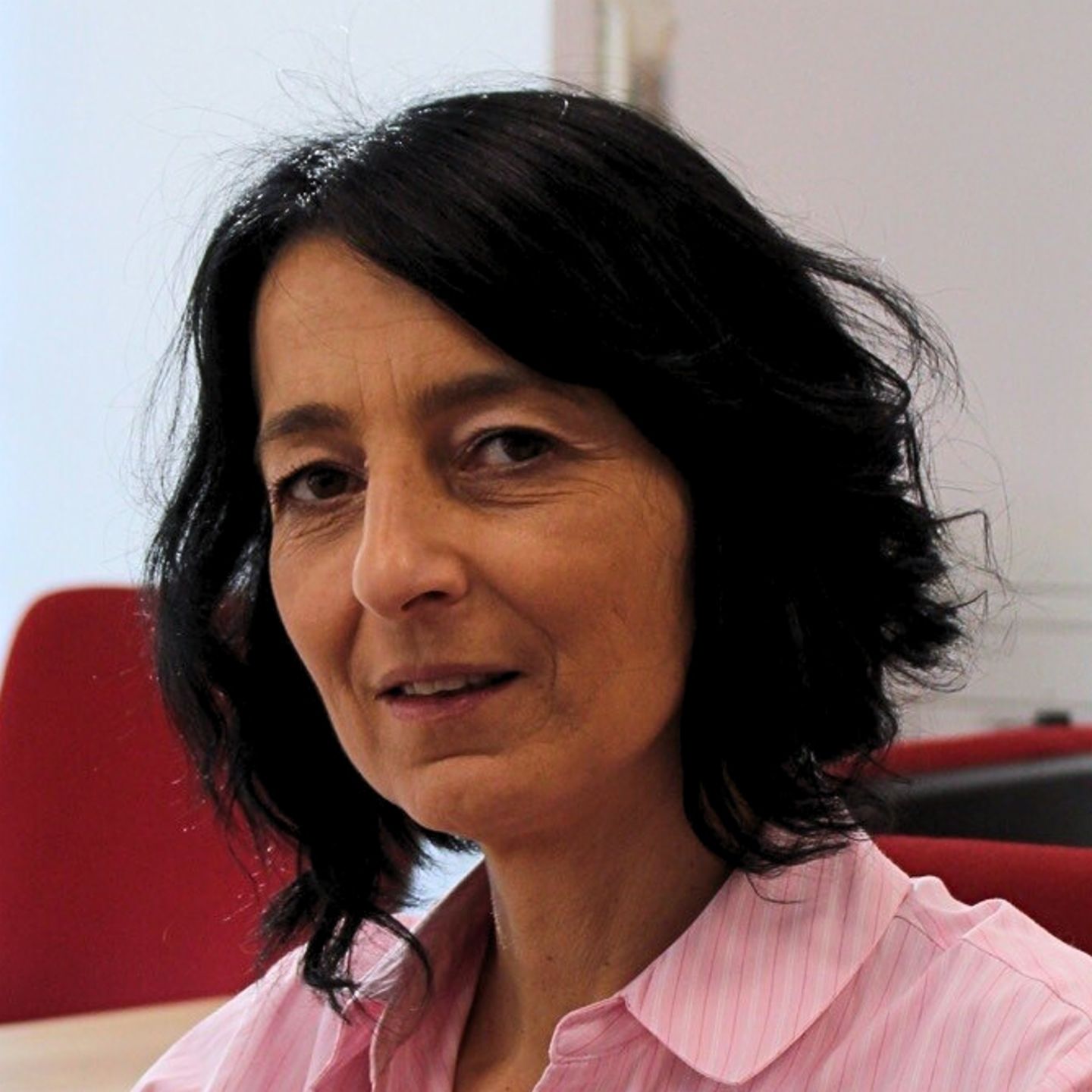 Cristina Pasere, kierownik ds. wsparcia operacji zgodności w EOS Rumunia, siedzi przy biurku w różowej bluzce w paski i patrzy w kamerę.