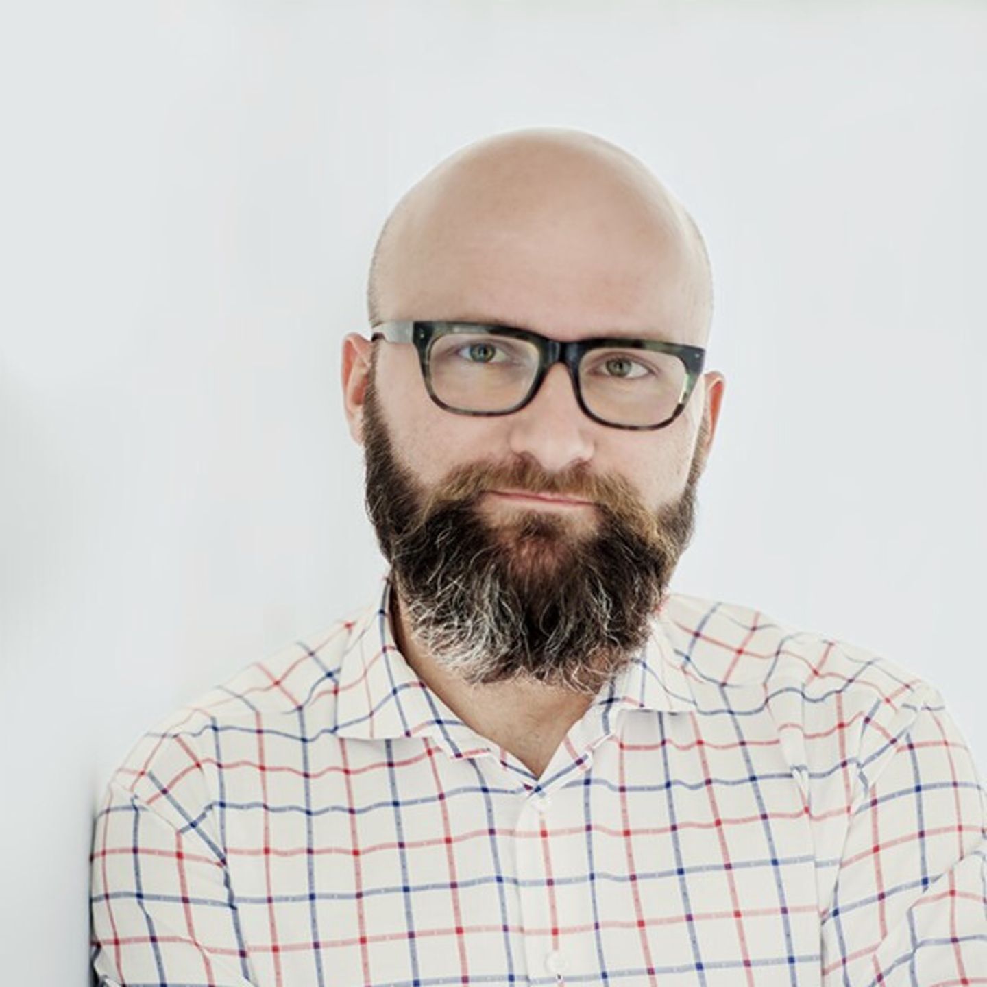 Dr hab. Tomasz Piekot w koszuli w kratę oparty o białą ścianę.
