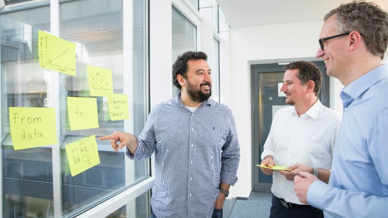 A project team discusses target groups around the whiteboard.