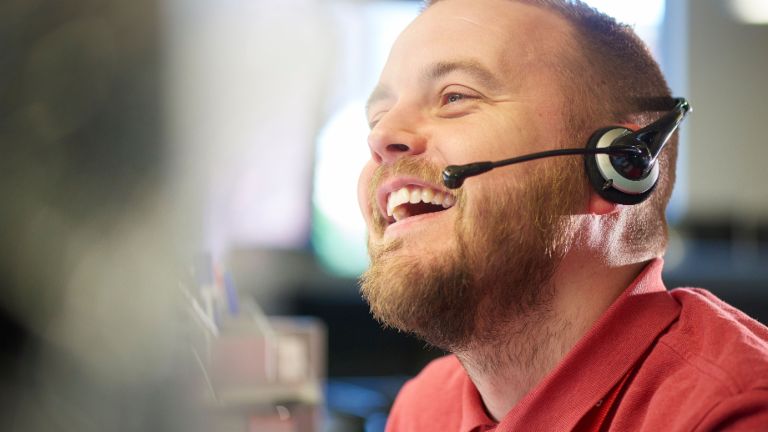 A young man with a headset smiles while on the phone.