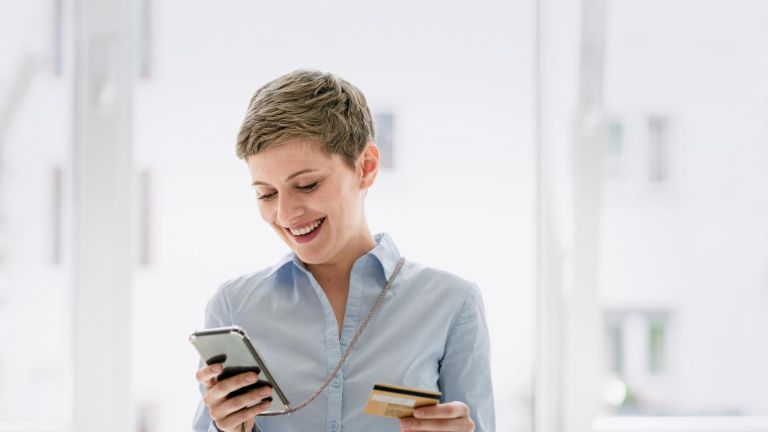 Woman with short hair looks at her mobile phone and has her credit card in the other hand. 