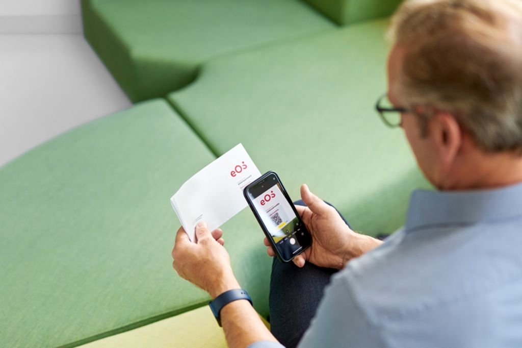 Mężczyzna skanuje kod QR na liście od EOS za pomocą smartfona, aby uregulować swoje otwarte roszczenie online na Portalu EOS.