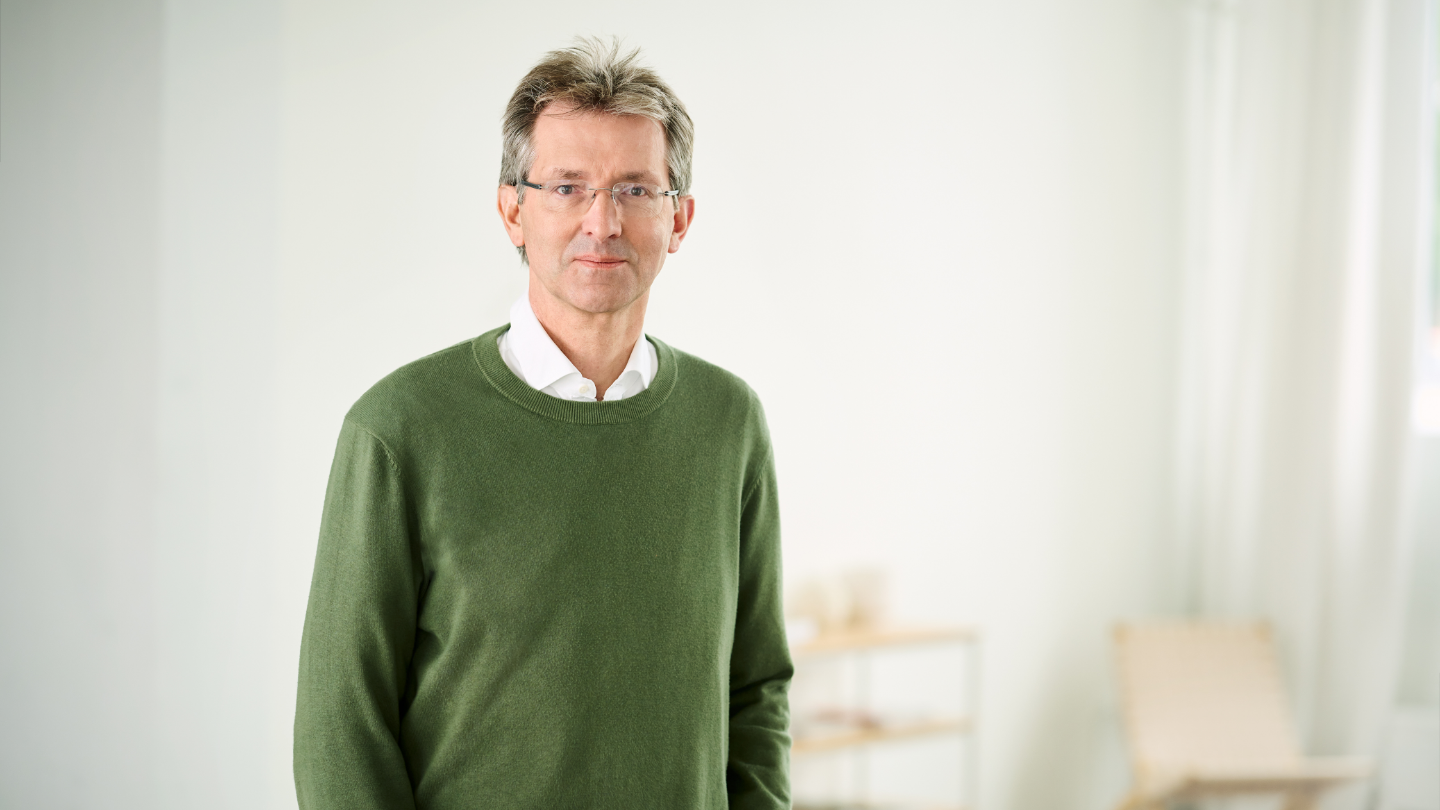 Justus Hecking-Veltman, CFO, w ciemnozielonym swetrze i białej koszuli stoi w jasnym pomieszczeniu.