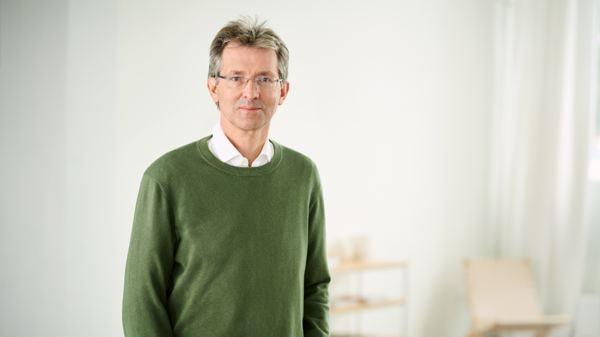 Justus Hecking-Veltman, CFO, w ciemnozielonym swetrze i białej koszuli stoi w jasnym pomieszczeniu.