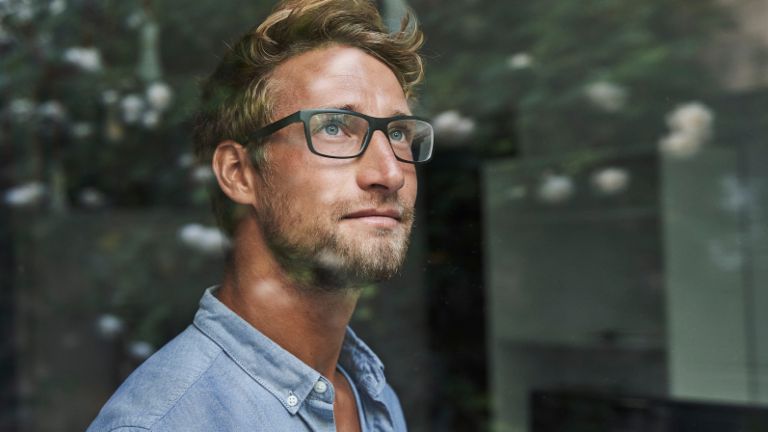 Młody mężczyzna z pokolenia Z z niepokojem wygląda przez okno.