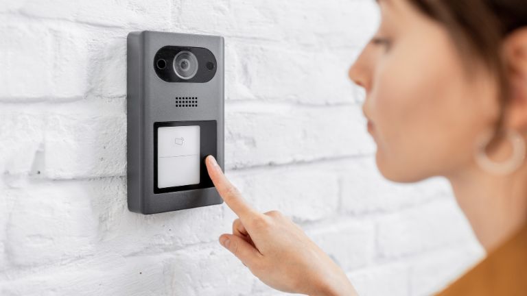Woman rings the house intercom with a camera installed on the white brick wall