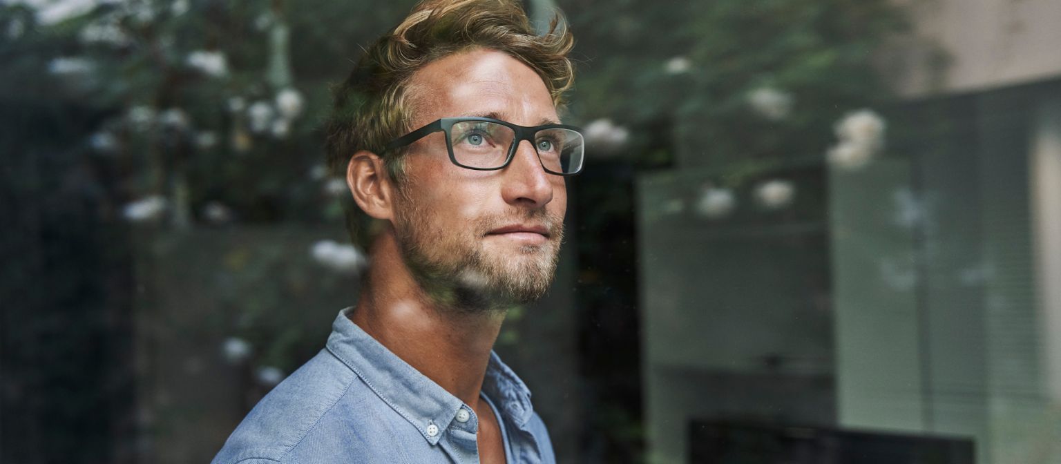 Młody mężczyzna z pokolenia Z z niepokojem wygląda przez okno.