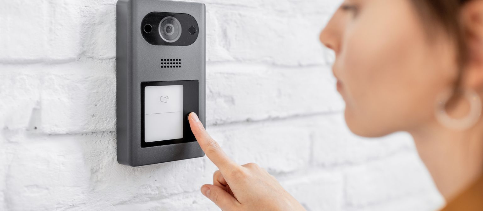 Woman rings the house intercom with a camera installed on the white brick wall