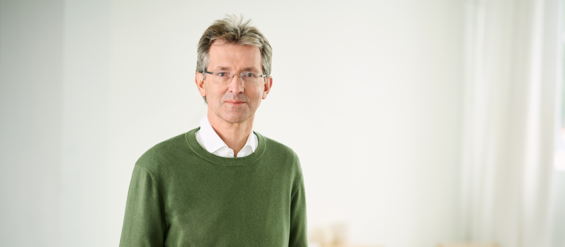 Justus Hecking-Veltman, CFO, w ciemnozielonym swetrze i białej koszuli stoi w jasnym pomieszczeniu.