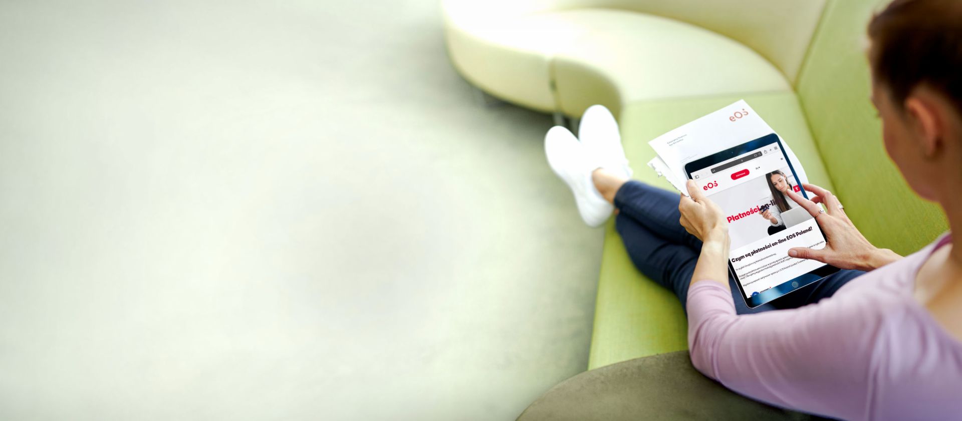 Kobieta korzysta z portalu internetowego EOS na tablecie, aby spłacić zaległe długi z wygodnej kanapy.