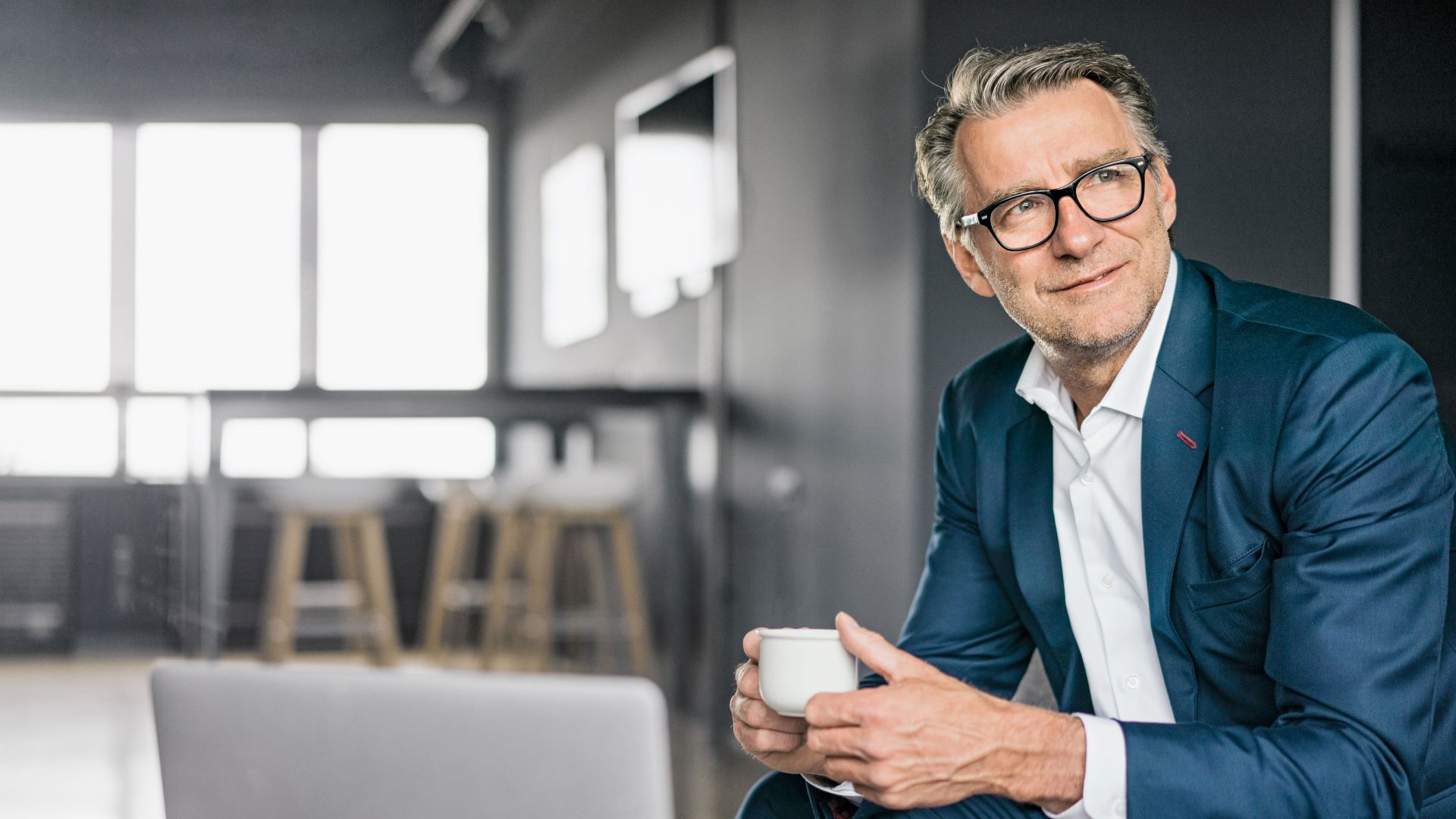 Portret siedzącego dojrzałego biznesmena w niebieskim garniturze, trzymającego białą filiżankę kawy