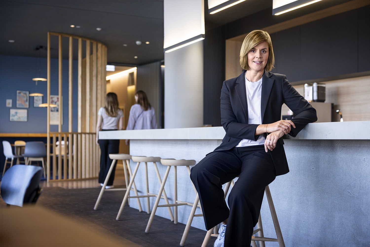 Dr. Eva Griewel, dyrektor finansowy (CFO) Grupy EOS, siedzi w przestrzeni społecznej na wysokim stołku, ubrana w czarny bleyzer.